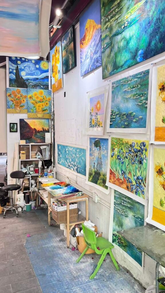 Inside a working artist's studio in Dafen, showing paints, brushes, and works in progress on the wall. Real hand-painted production.